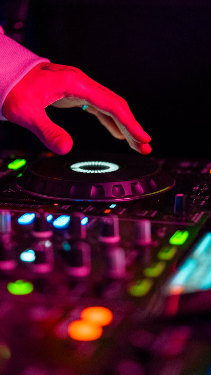 Close-up of a DJ's hand mixing music in a vibrant club setting under colorful lights.