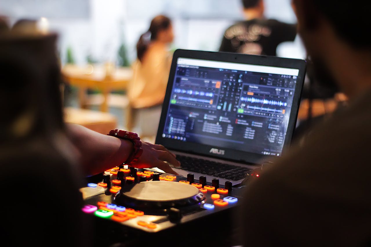 DJ mixing music using a laptop and mixer in a lively cafe setting with people in the background.