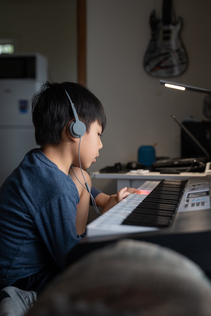 services-02 Young boy wearing headphones, playing the keyboard indoors, immersed in music.