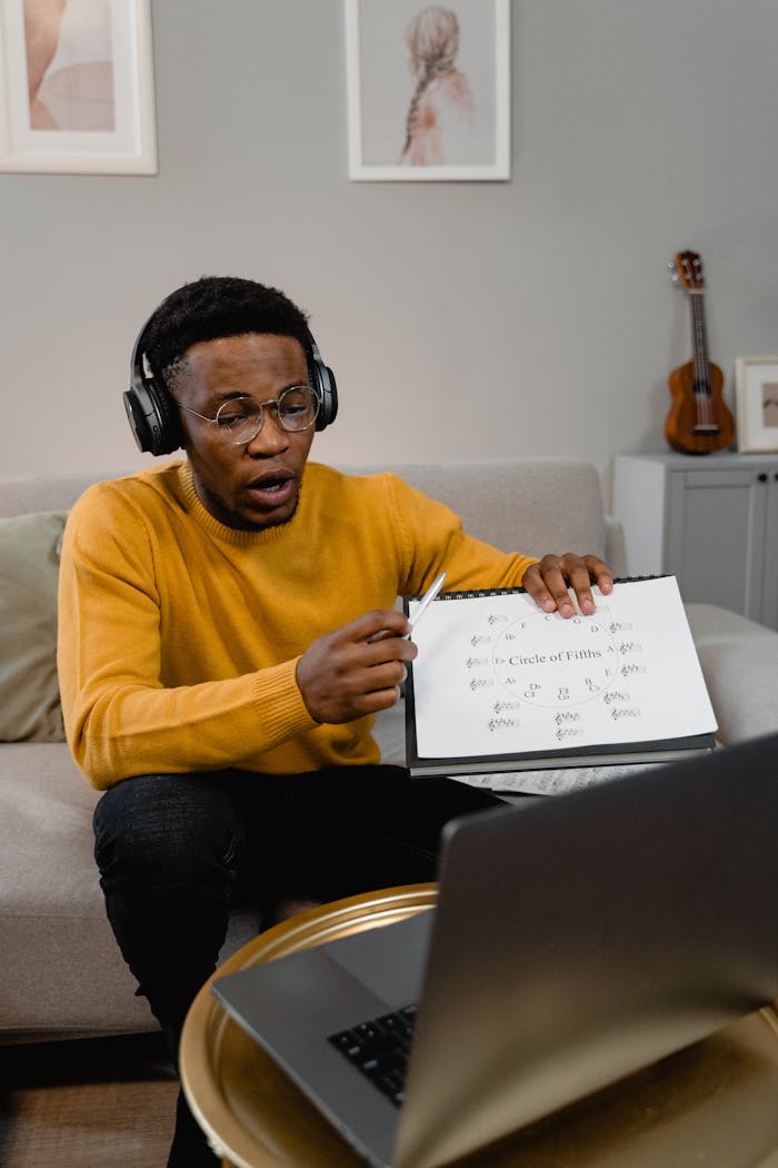 about-bg A man teaching music online, wearing headphones and holding a notebook, in a cozy home setting.