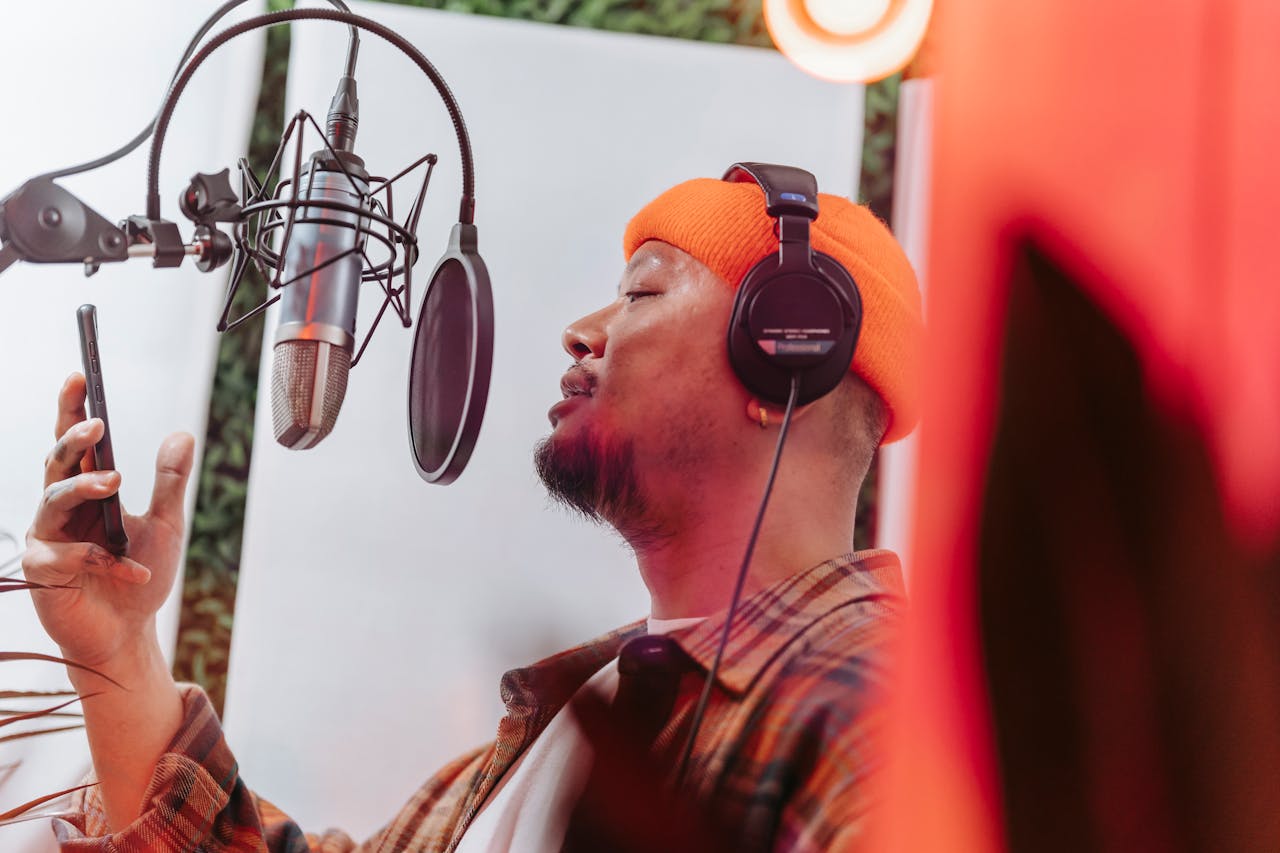 A young musician passionately singing in a recording studio with headphones and microphone setup.